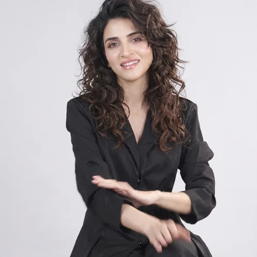 A woman with a voluminous, shoulder-length 80s curly shag haircut. The hairstyle features heavily layered, definition-rich curls with a deep side part that builds height at the crown. Shorter, textured face-framing layers taper downwards around her cheeks and jawline, blending seamlessly into longer curly lengths.