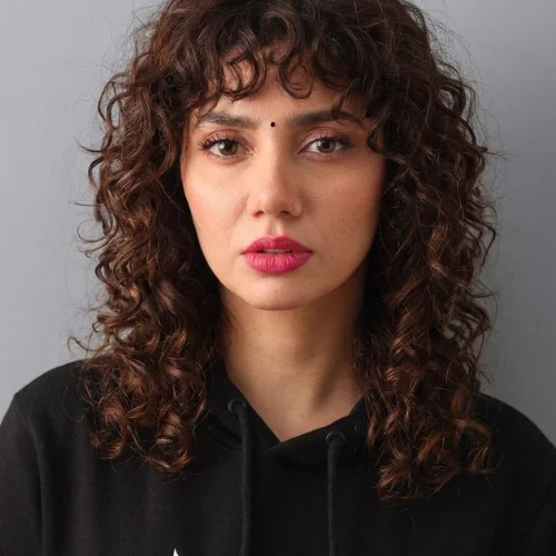 Woman with a curly jellyfish wolf cut and full curly bangs.