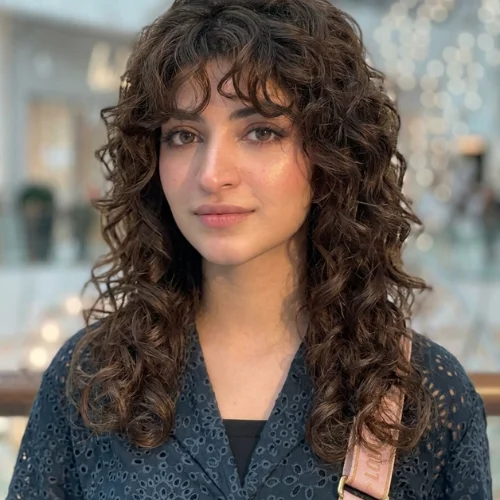 "Curly mullet wolf haircut with textured layers, soft curly bangs, and defined curls for a bold modern shag style."